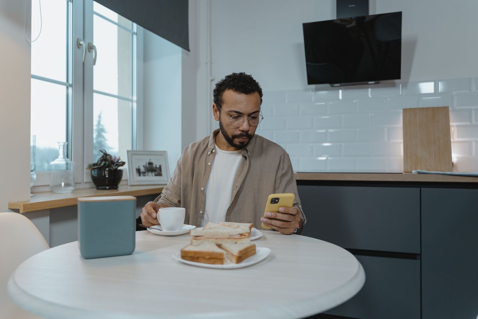Mann frühstückt in der Küche und schaut auf sein Handy